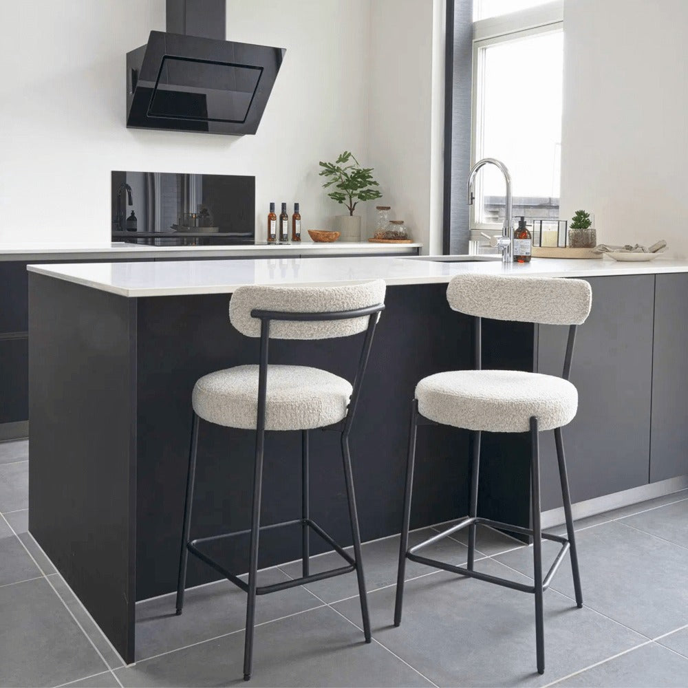 Moderne Badalona barkruk met witte bouclé bekleding en zwarte metalen poten aan een zwart keukeneiland, interieurinspiratie van House Nordic.