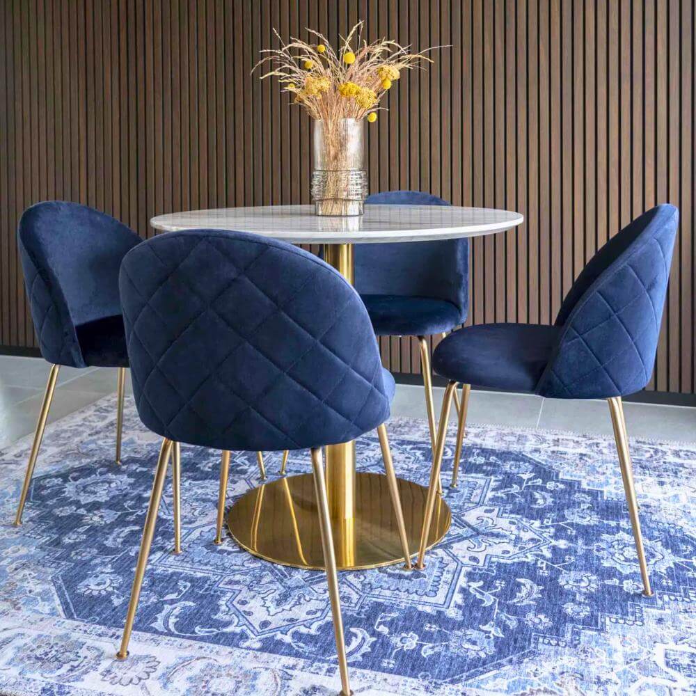 Vier donkerblauwe velvet Geneve eetkamerstoelen van House Nordic met gouden poten rond een marmeren eettafel in een elegant modern interieur – productfoto van Lunero.