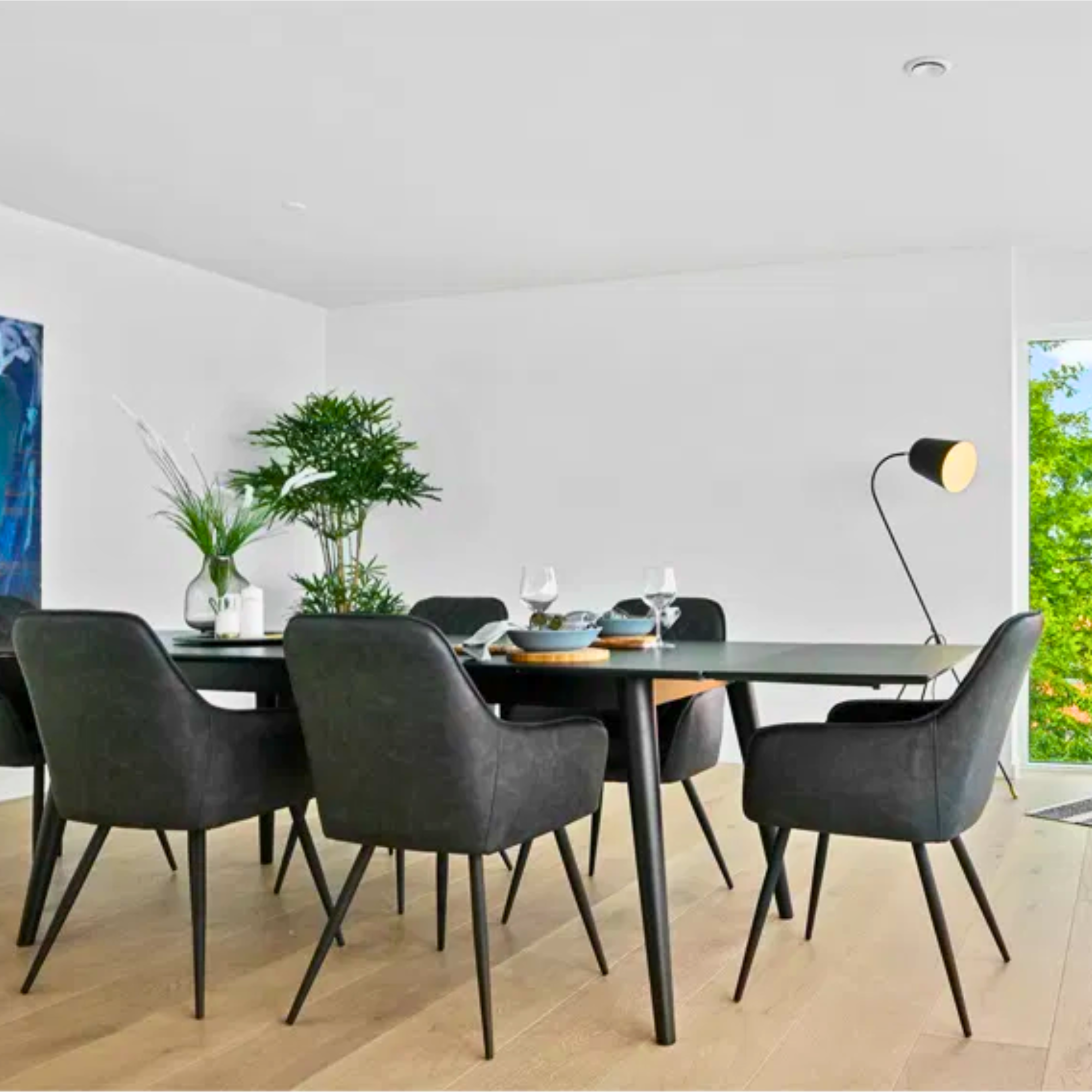 Donkergrijze House Nordic Harbo eetkamerstoel met zwarte poten rond een moderne eettafel in een Scandinavisch interieur met houten vloer en groene accenten.