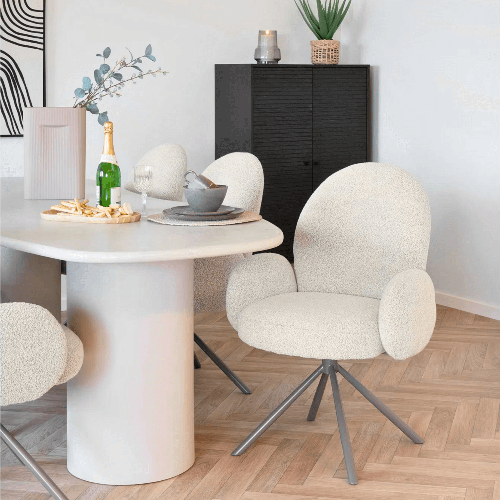 Twee House Nordic Lana eetkamerstoelen met armleuningen in zandkleurige bouclé stof aan een ronde eettafel in Scandinavisch interieur.