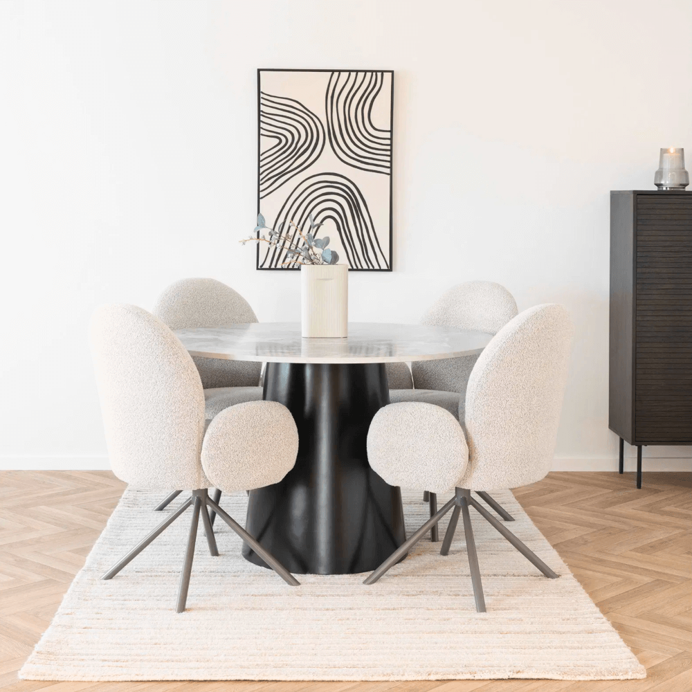 Vier House Nordic Lana eetkamerstoelen met armleuningen in zandkleurige bouclé stof rond een ronde eettafel in Scandinavisch interieur.