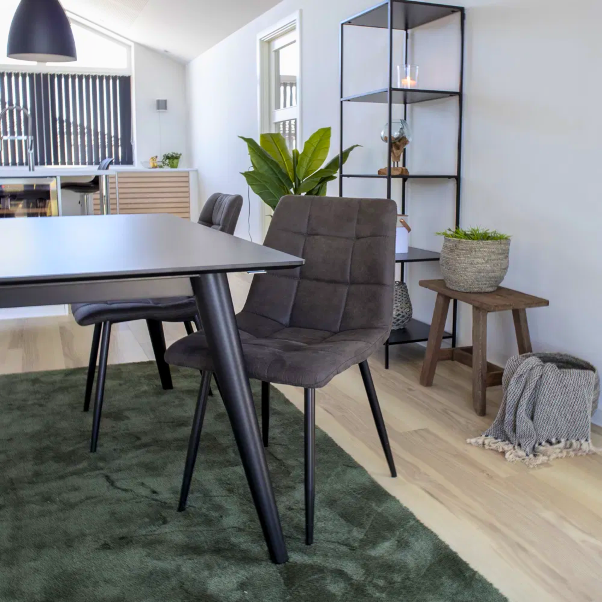 House Nordic Middelfart eetkamerstoel in donkergrijs microvezel met zwarte poten aan zwarte eettafel op groen vloerkleed in modern interieur.