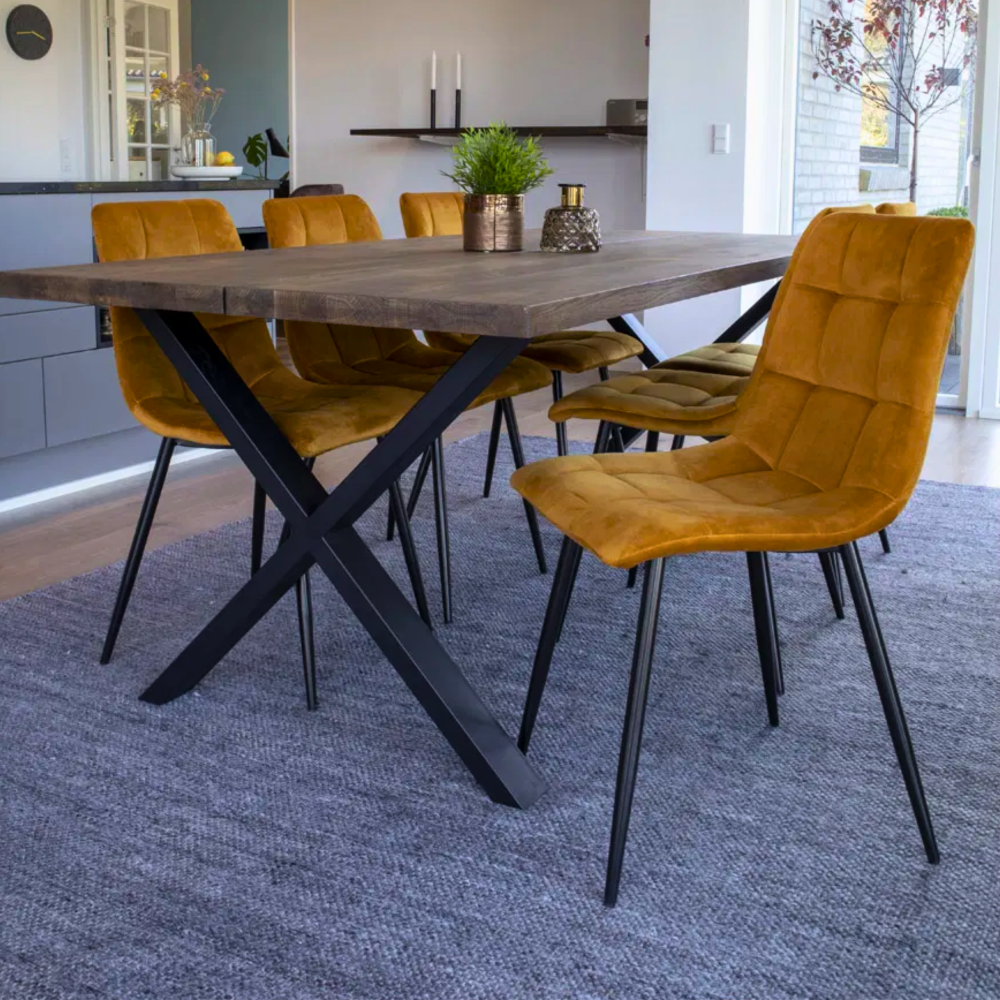 Close-up van House Nordic Middelfart eetkamerstoelen in geel velvet met zwarte metalen poten aan houten eettafel.