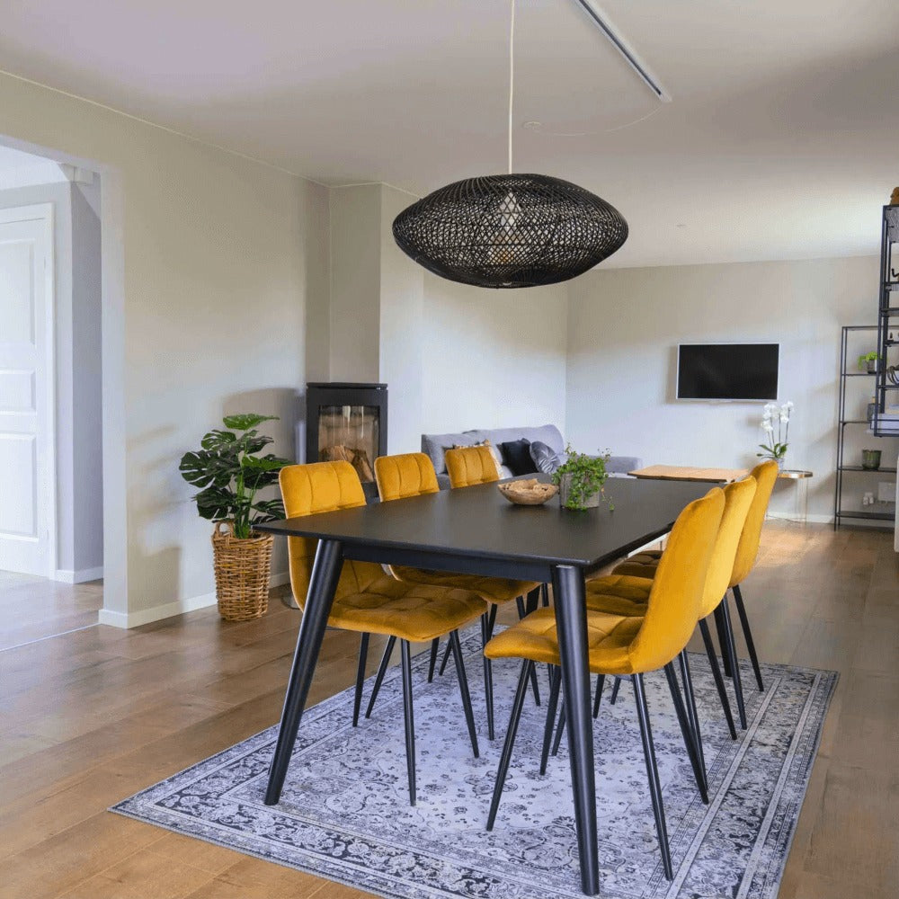 Moderne eetkamer met House Nordic Middelfart eetkamerstoelen in geel velvet met zwarte poten rond zwarte eettafel in Scandinavisch interieur.
