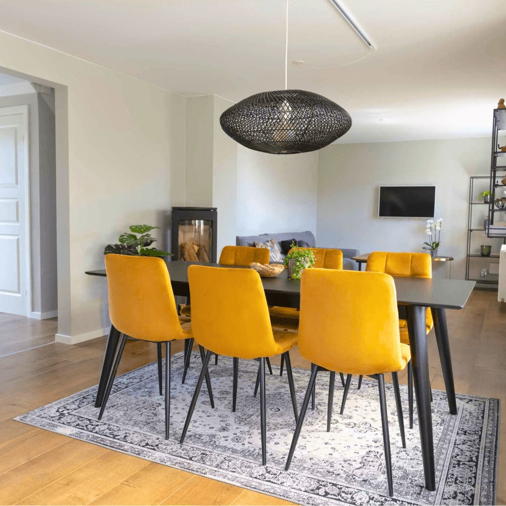 Scandinavisch ingerichte woonkamer met House Nordic Middelfart eetkamerstoelen in geel velvet met zwarte poten aan zwarte eettafel.