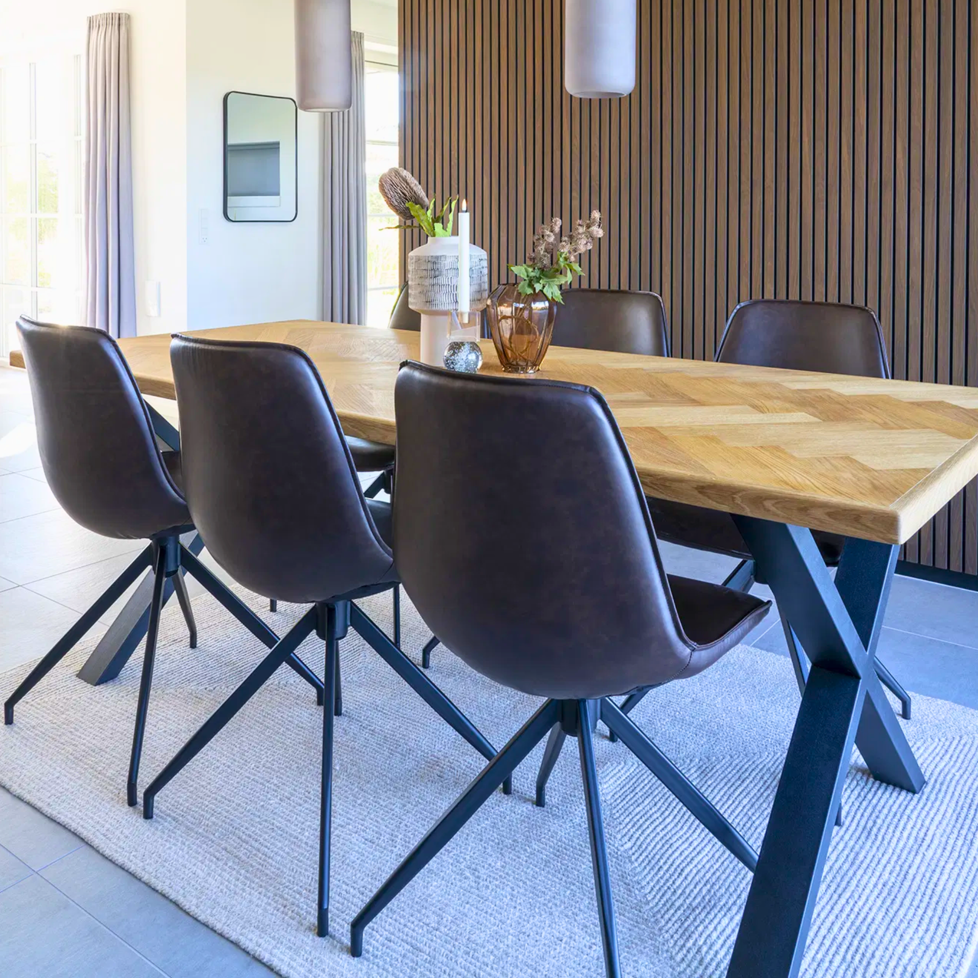 Achteraanzicht van de Monaco eetkamerstoelen van House Nordic in donkerbruin PU-leer met zwarte metalen poten, geplaatst rond een houten eettafel in modern interieur.