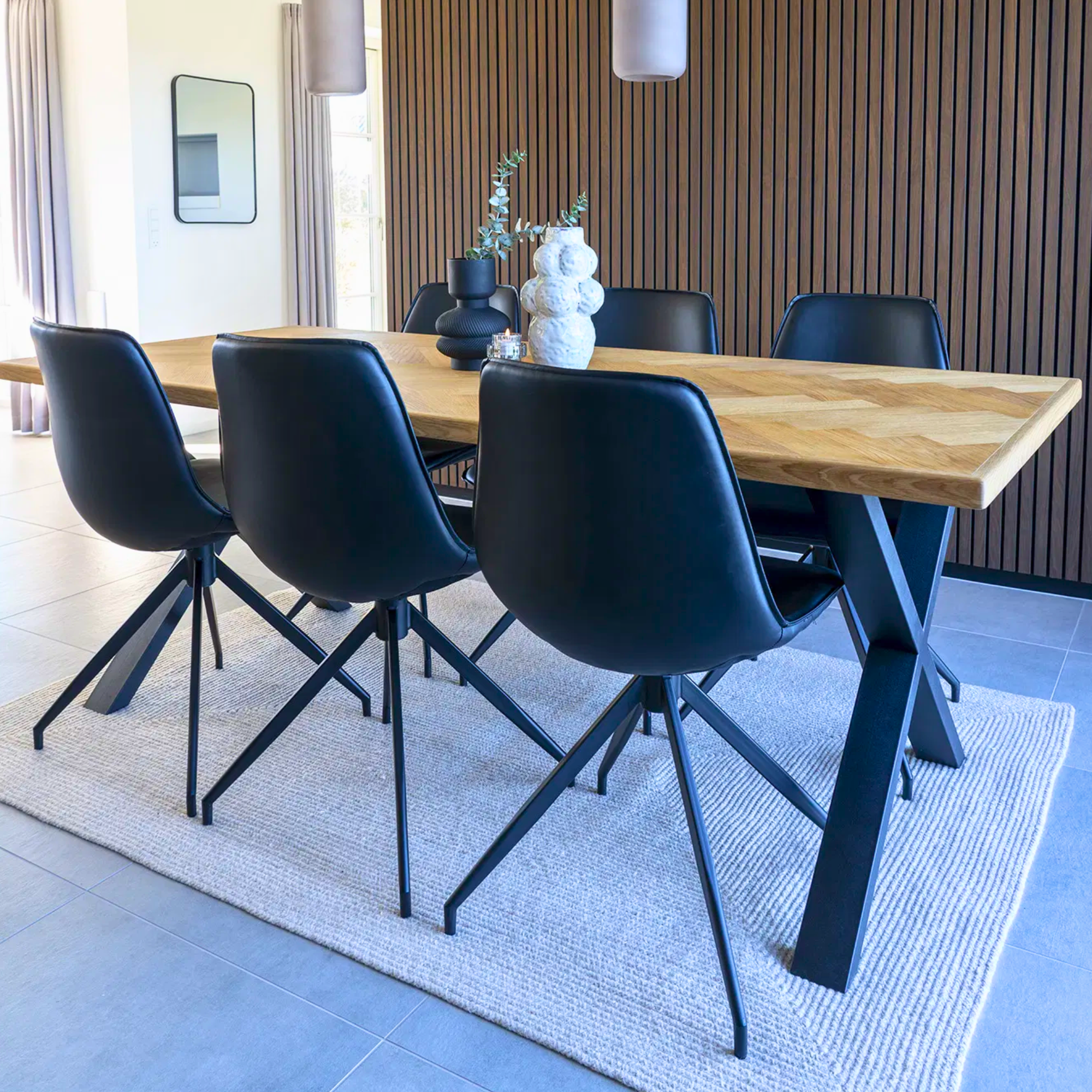 Achteraanzicht van de Monaco eetkamerstoelen van House Nordic in zwart PU-leer met zwarte metalen poten, geplaatst rond een houten eettafel in modern interieur.