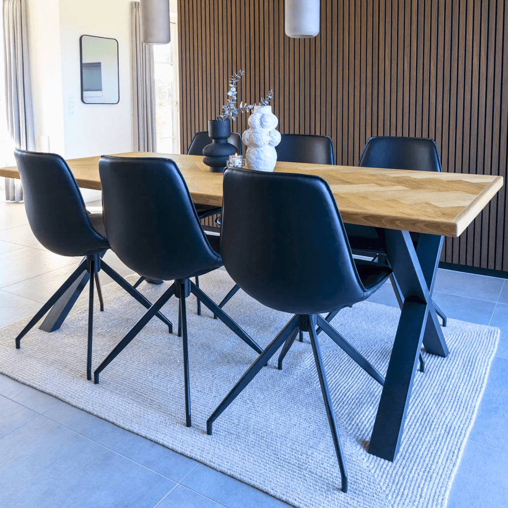 Achteraanzicht van de Monaco eetkamerstoelen van House Nordic in zwart PU-leer met zwarte metalen poten, geplaatst rond een houten eettafel in modern interieur.