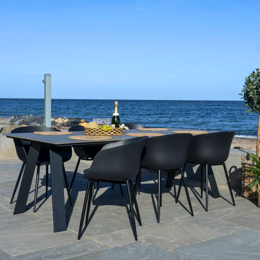 Zwarte House Nordic Roda eetkamerstoelen rond buitentafel met uitzicht op zee – elegant Scandinavisch design voor terras of tuin.