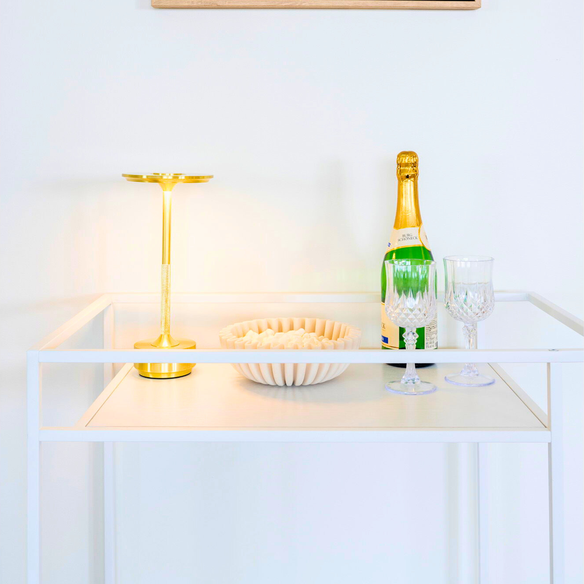 House Nordic Vita serveerwagen in wit met champagnefles, glazen en gouden tafellamp – stijlvolle drankentrolley in Scandinavisch design.