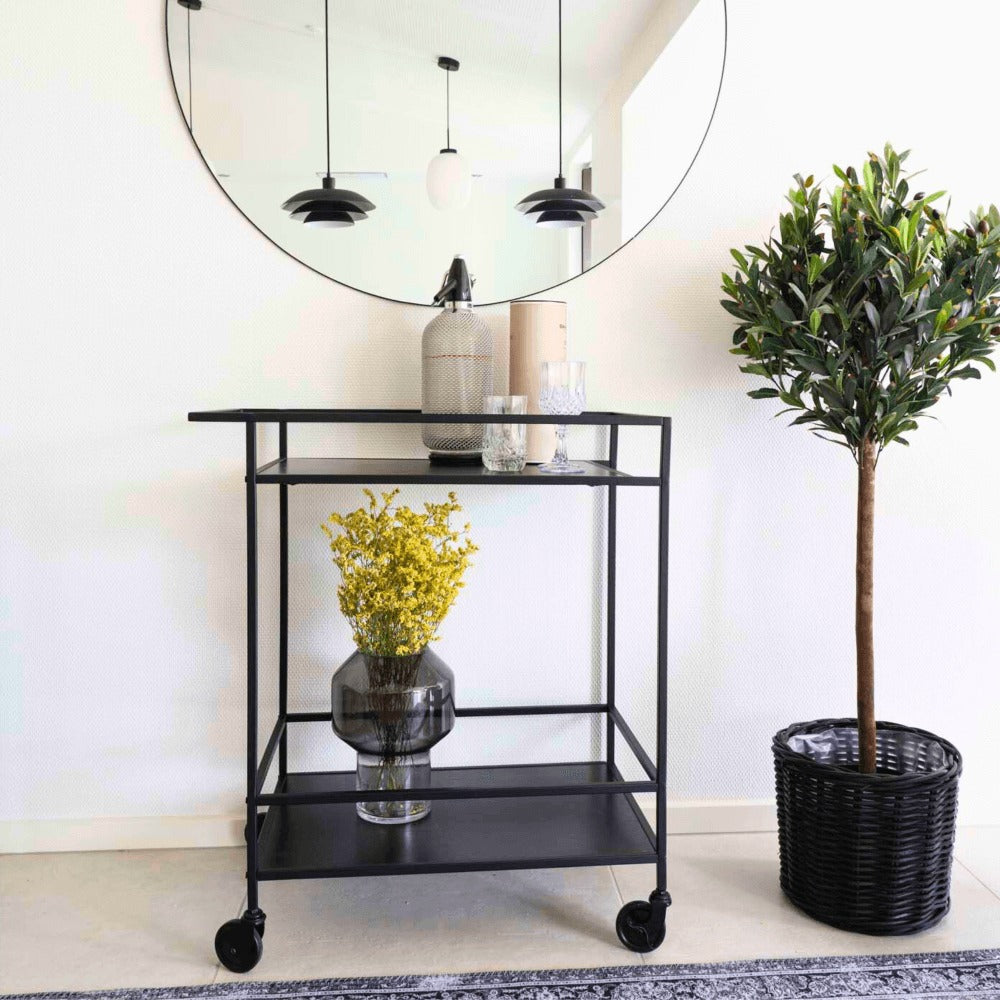 House Nordic Vita serveerwagen in zwart met bloemenvaas, glazen en decoratie in Scandinavisch interieur met spiegel en kamerplant.