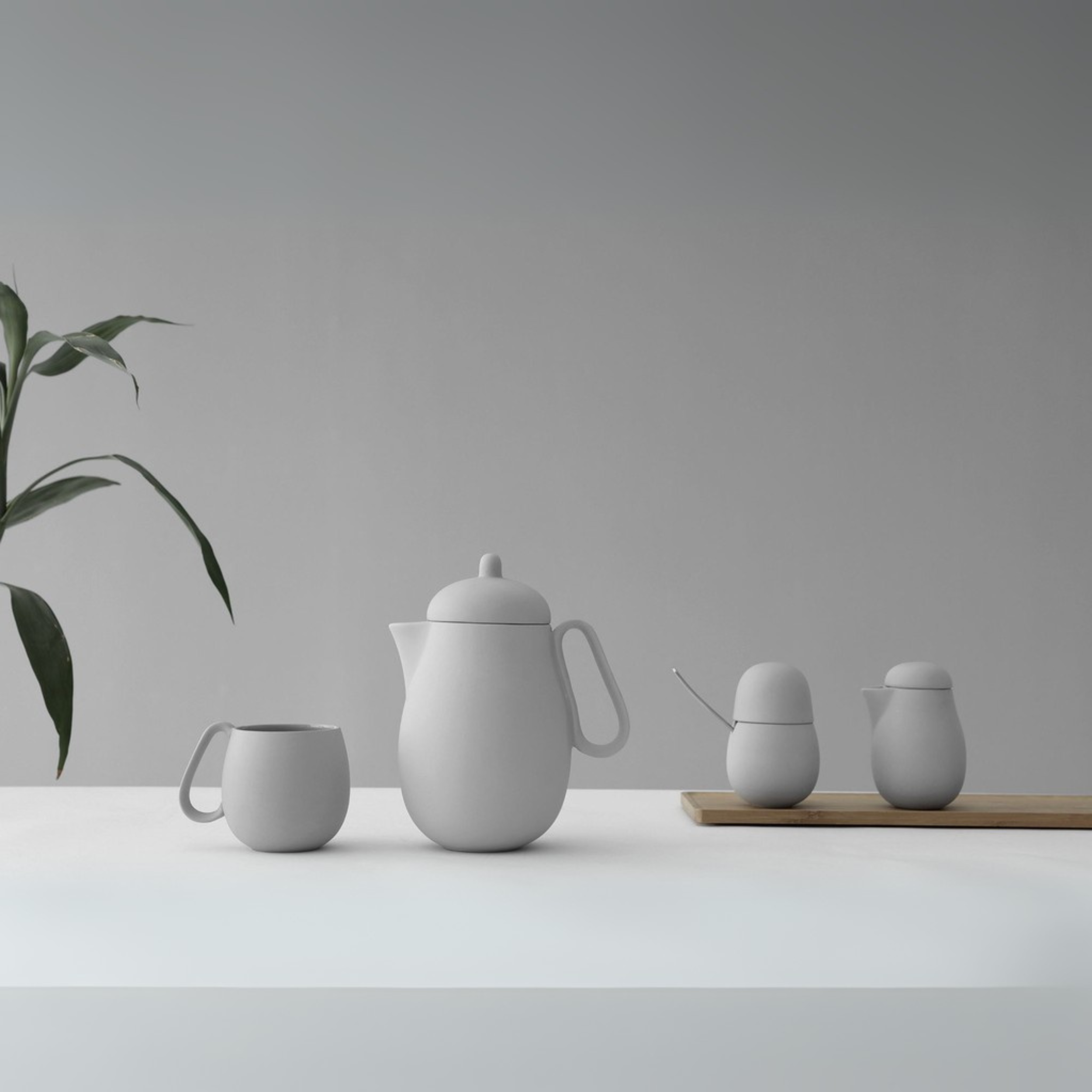 Minimalistische witte keramische theeset met theepot, kopje, suikerpot en melkkan op tafel met houten serveerplank.