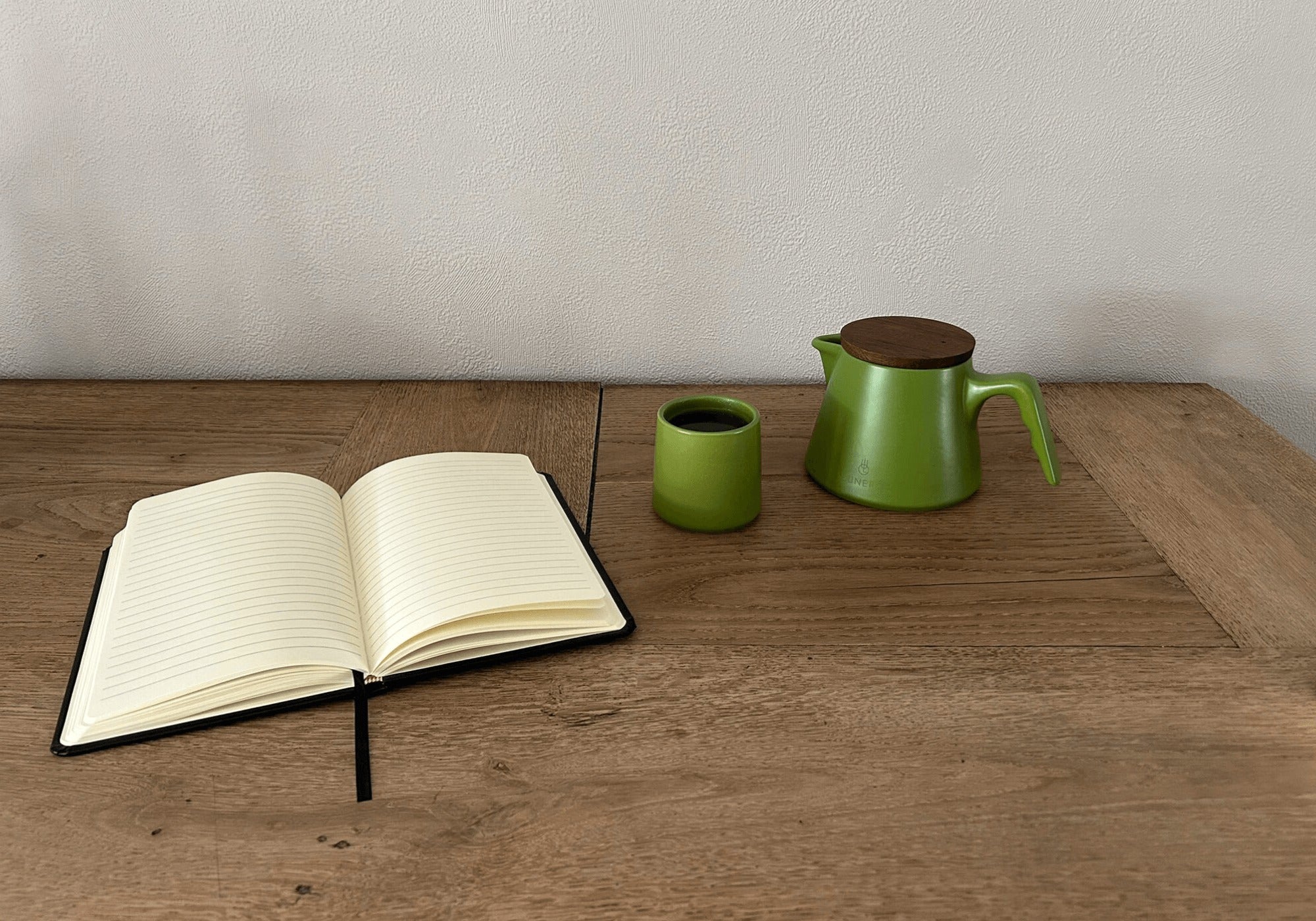 Groene Lunero theeset met houten deksel en kopje, naast een open notitieboek op houten tafel – stijlvolle en serene lifestyle setting.