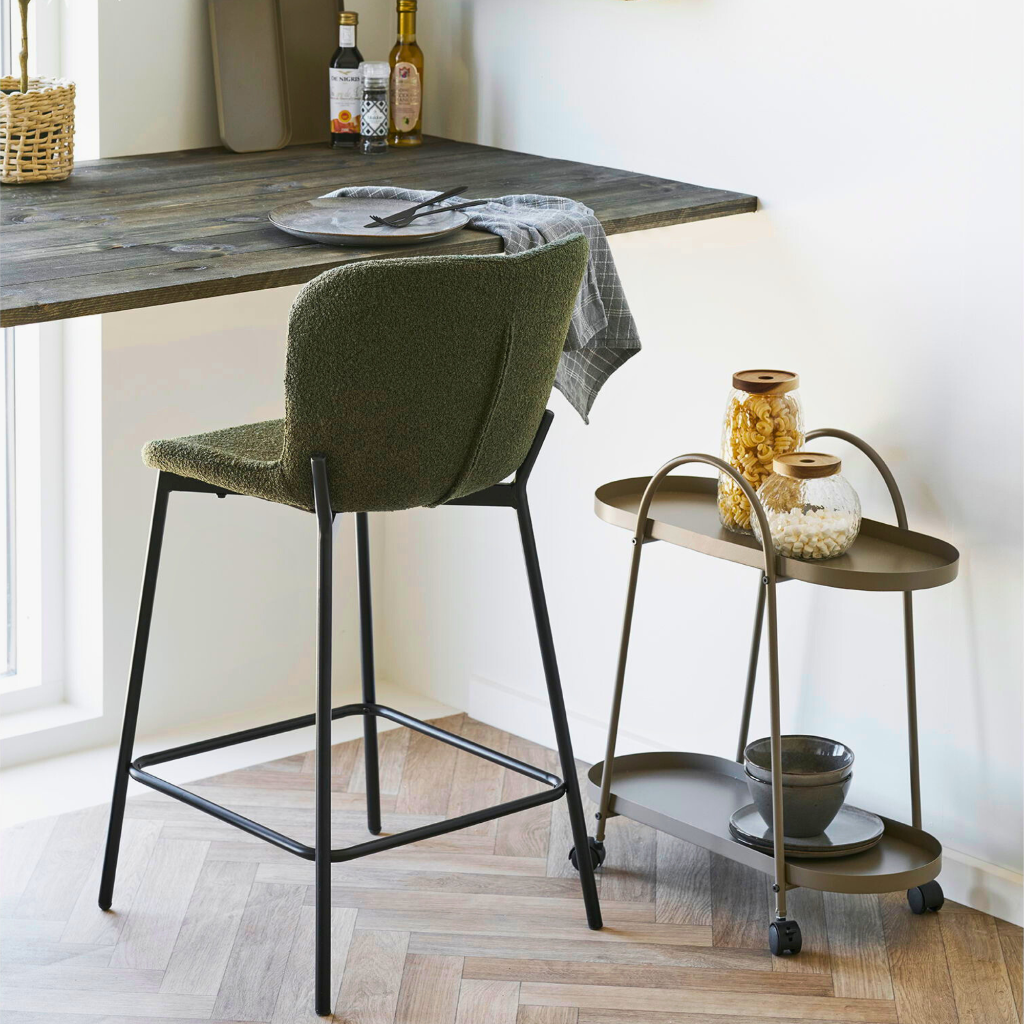 Maceda barkruk in donkergroen bouclé met zwarte poten, geplaatst aan een houten bar in een modern Scandinavisch interieur van House Nordic.