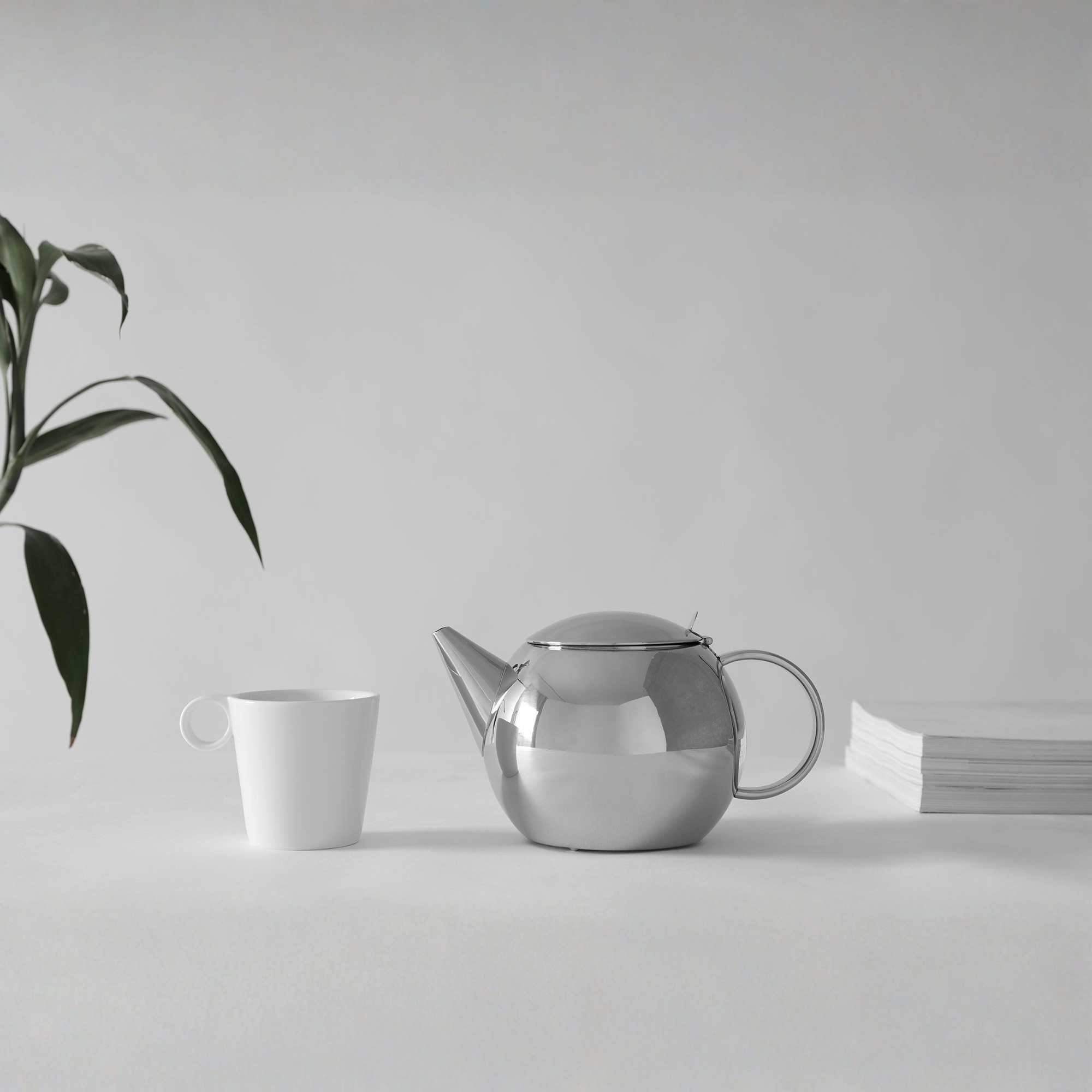 Viva Scandinavia Lucas theepot van roestvrij staal met witte mok en plant op tafel – minimalistisch Scandinavisch interieur.