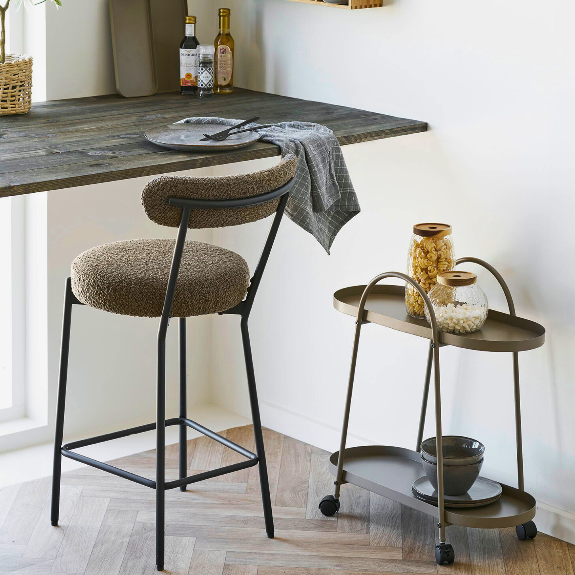 Stijlvolle Badalona barkruk met bouclé bekleding en zwarte metalen poten aan een houten bartafel, modern interieur bij Lunero.