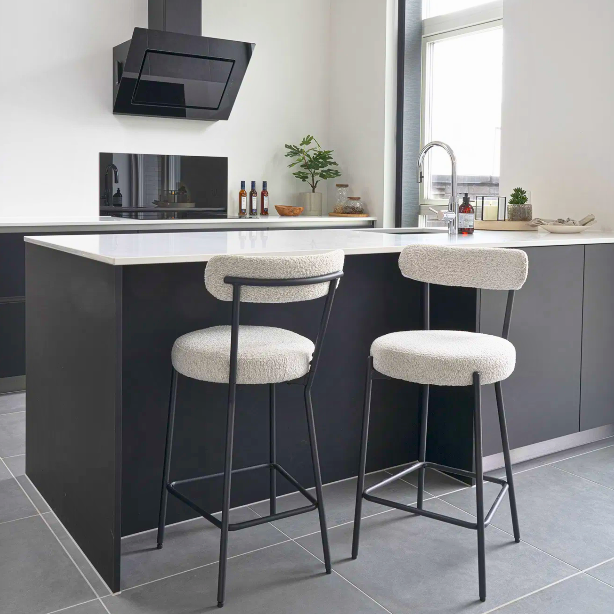 Moderne Badalona barkruk met witte bouclé bekleding en zwarte metalen poten aan een zwart keukeneiland, interieurinspiratie van House Nordic.