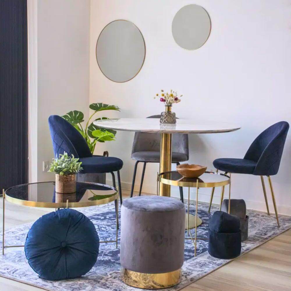 Donkerblauwe velvet eetkamerstoelen met gouden poten van House Nordic, stijlvol geplaatst aan een ronde eettafel in een modern Scandinavisch interieur – verkrijgbaar bij Lunero.