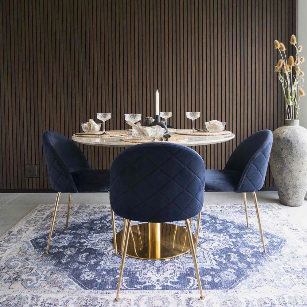 Donkerblauwe velvet Geneve eetkamerstoelen van House Nordic met gouden poten rond een ronde marmeren eettafel in een modern chique interieur – sfeervolle dining setting bij Lunero.