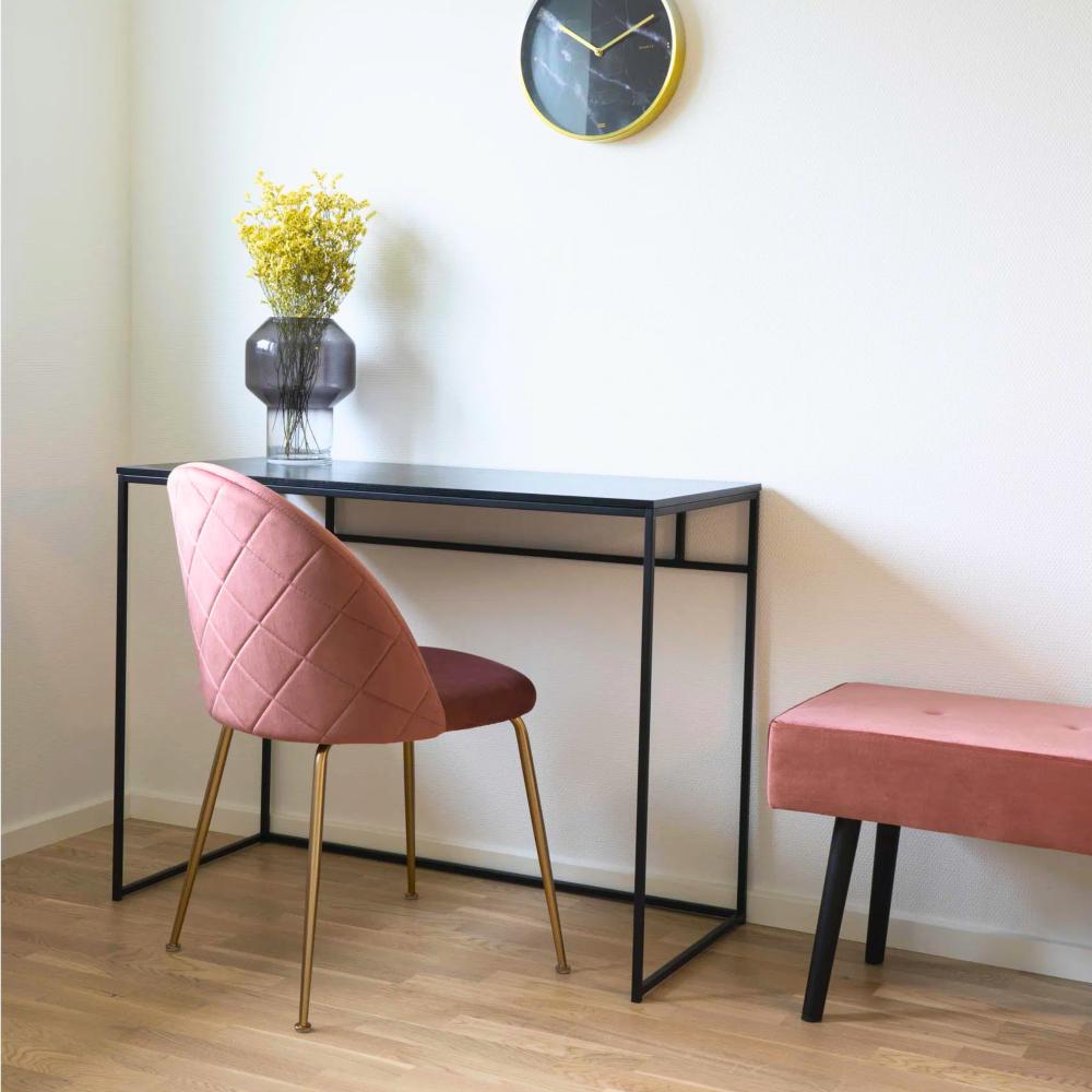 Roze velvet House Nordic Geneve eetkamerstoel met gouden poten bij een zwarte tafel in een modern Scandinavisch interieur met houten vloer.