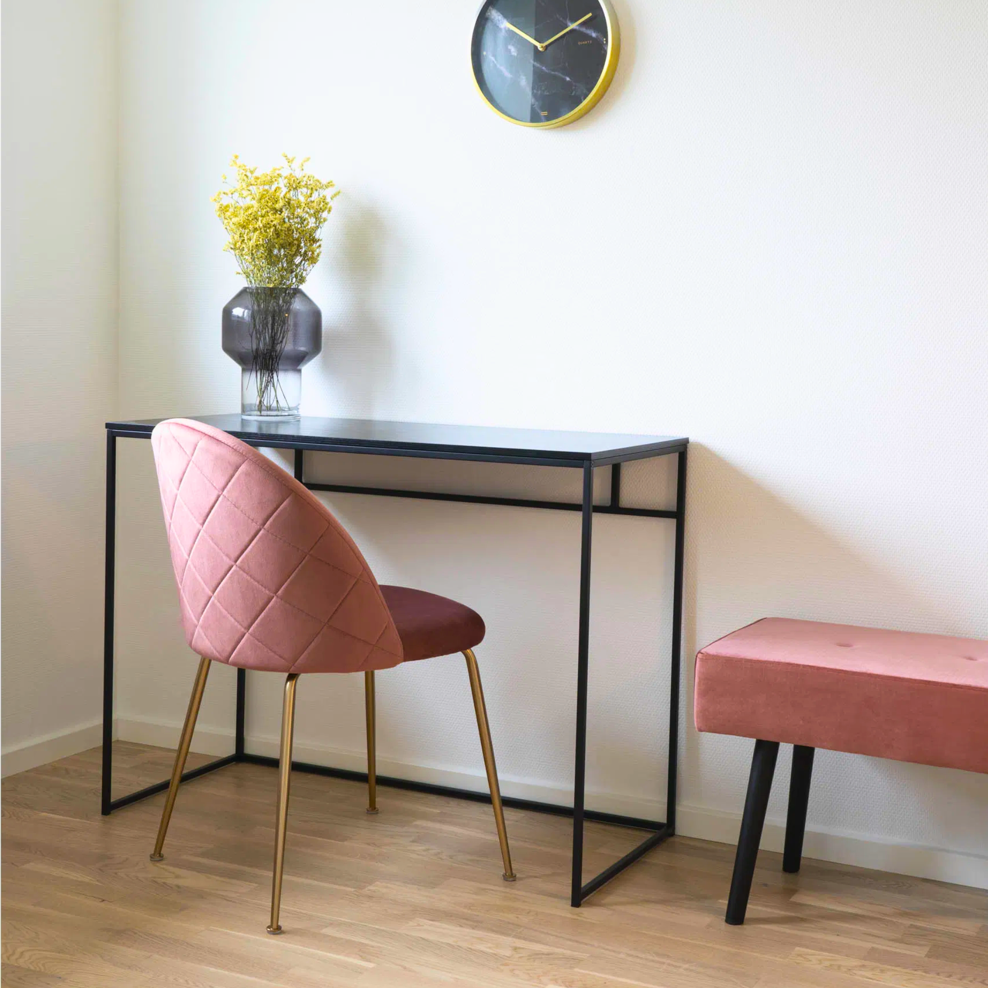 Roze velvet House Nordic Geneve eetkamerstoel met gouden poten bij een zwarte tafel in een modern Scandinavisch interieur met houten vloer.