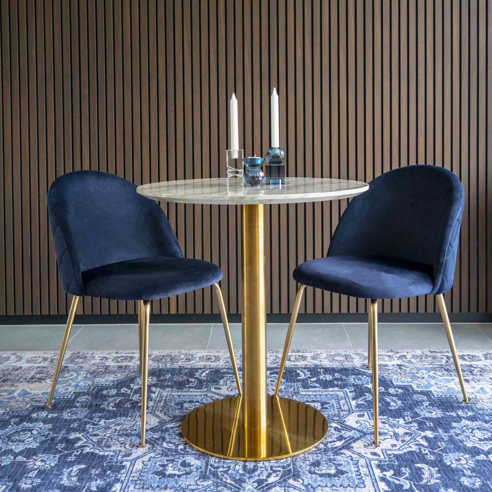 Set van twee donkerblauwe velvet Geneve eetkamerstoelen van House Nordic met gouden poten, geplaatst aan een marmeren eettafel met gouden voet in een modern interieur – productfoto van Lunero.