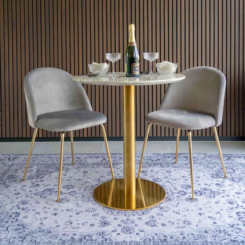 Twee grijs velvet House Nordic Geneve eetkamerstoelen met gouden poten aan een marmeren eettafel in modern interieur met houten wand.
