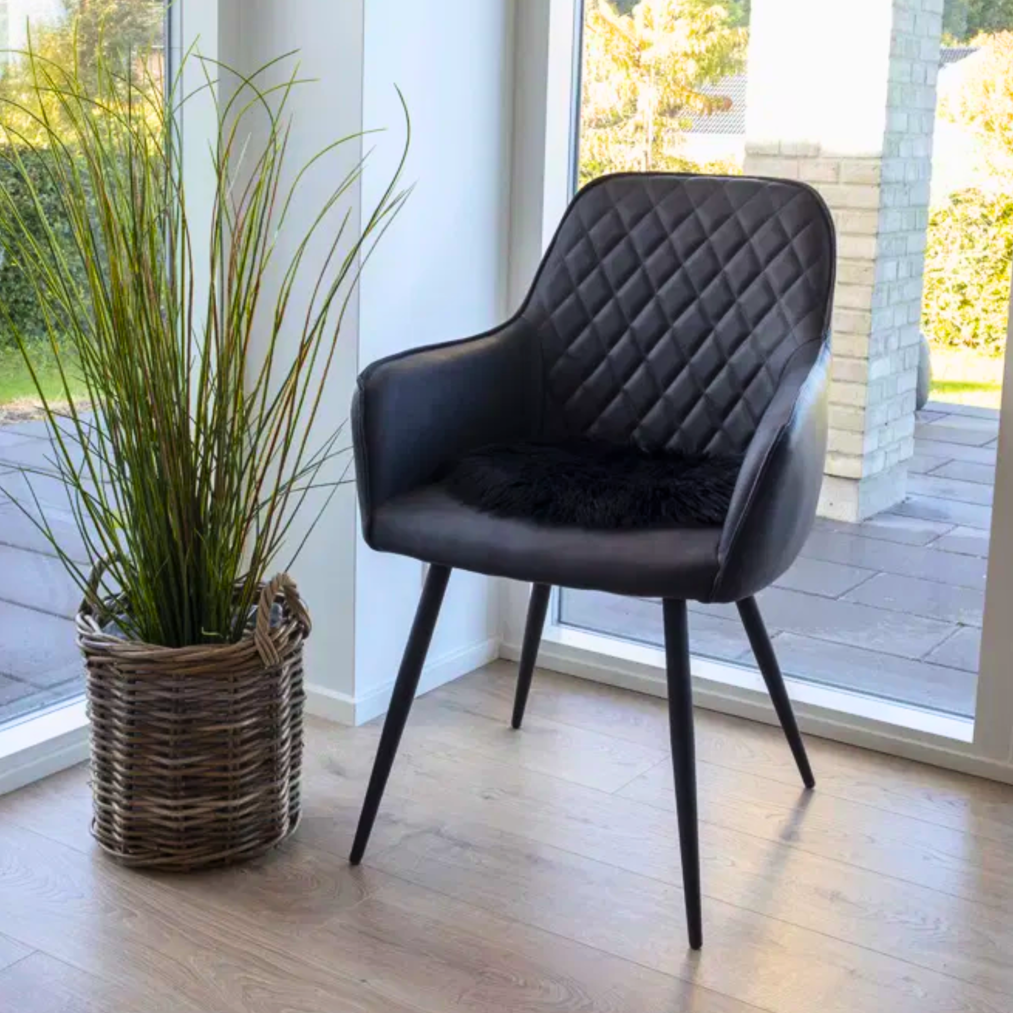 Zwarte House Nordic Harbo eetkamerstoel in modern interieur – PU-leren eetkamerstoel met ruitpatroon en zwarte poten naast een rotan plantmand.