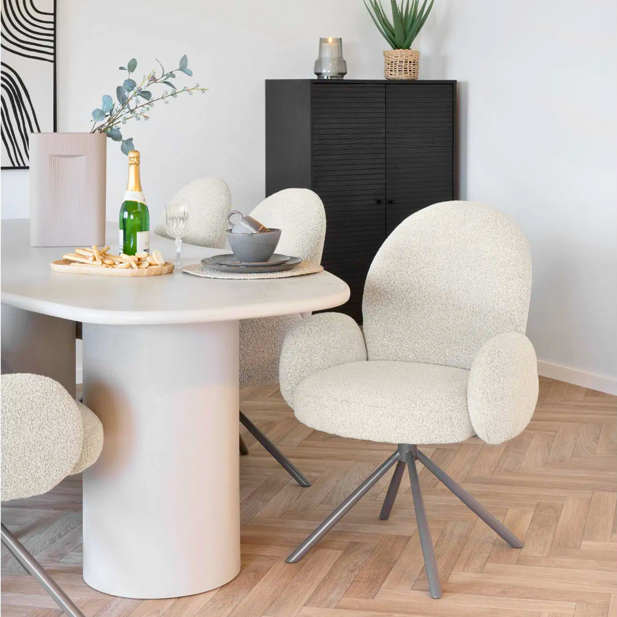 Twee House Nordic Lana eetkamerstoelen met armleuningen in zandkleurige bouclé stof aan een ronde eettafel in Scandinavisch interieur.