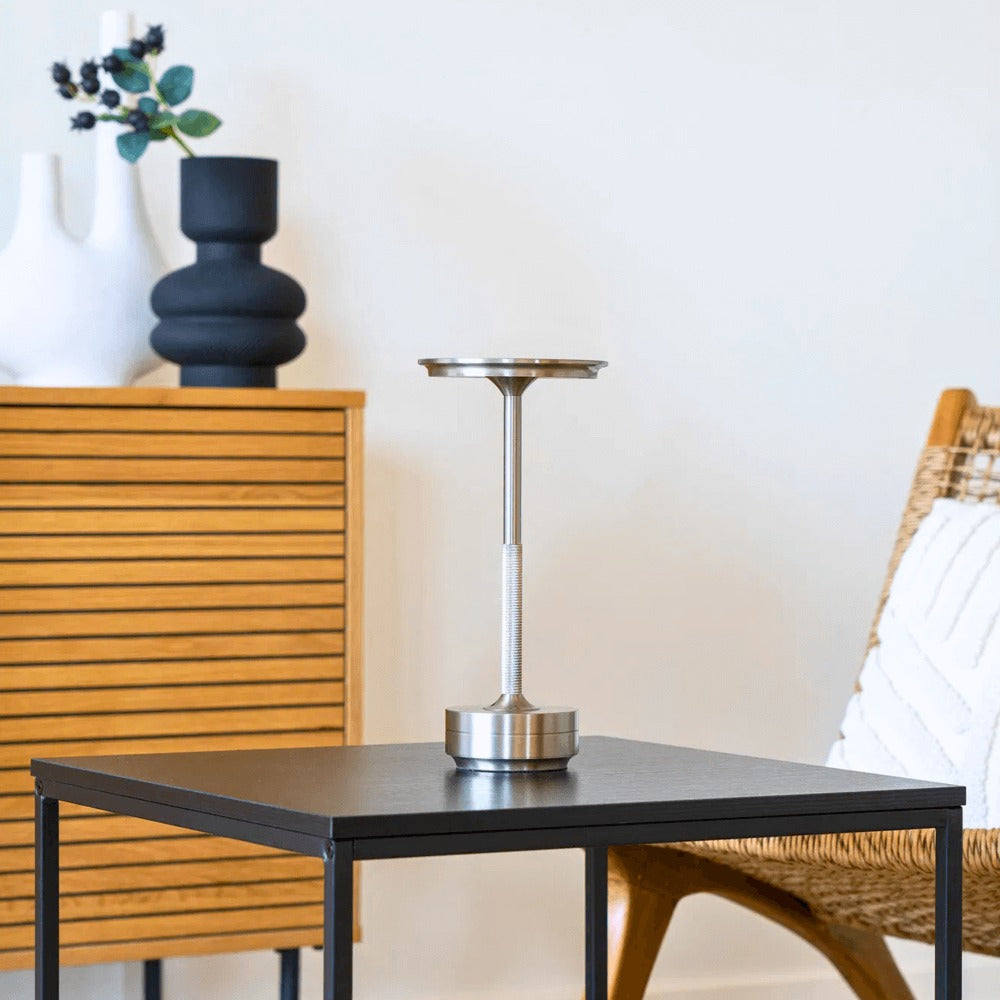 Zilveren Lyneham LED tafellamp van House Nordic op een zwarte bijzettafel in een modern Scandinavisch interieur met houtaccenten.