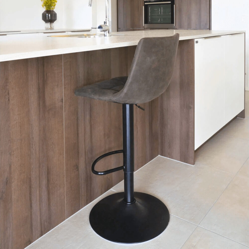 House Nordic Middelfart barkruk in donkergrijs microvezel met zwarte metalen poot, geplaatst aan houten keukeneiland in moderne interieurstijl.