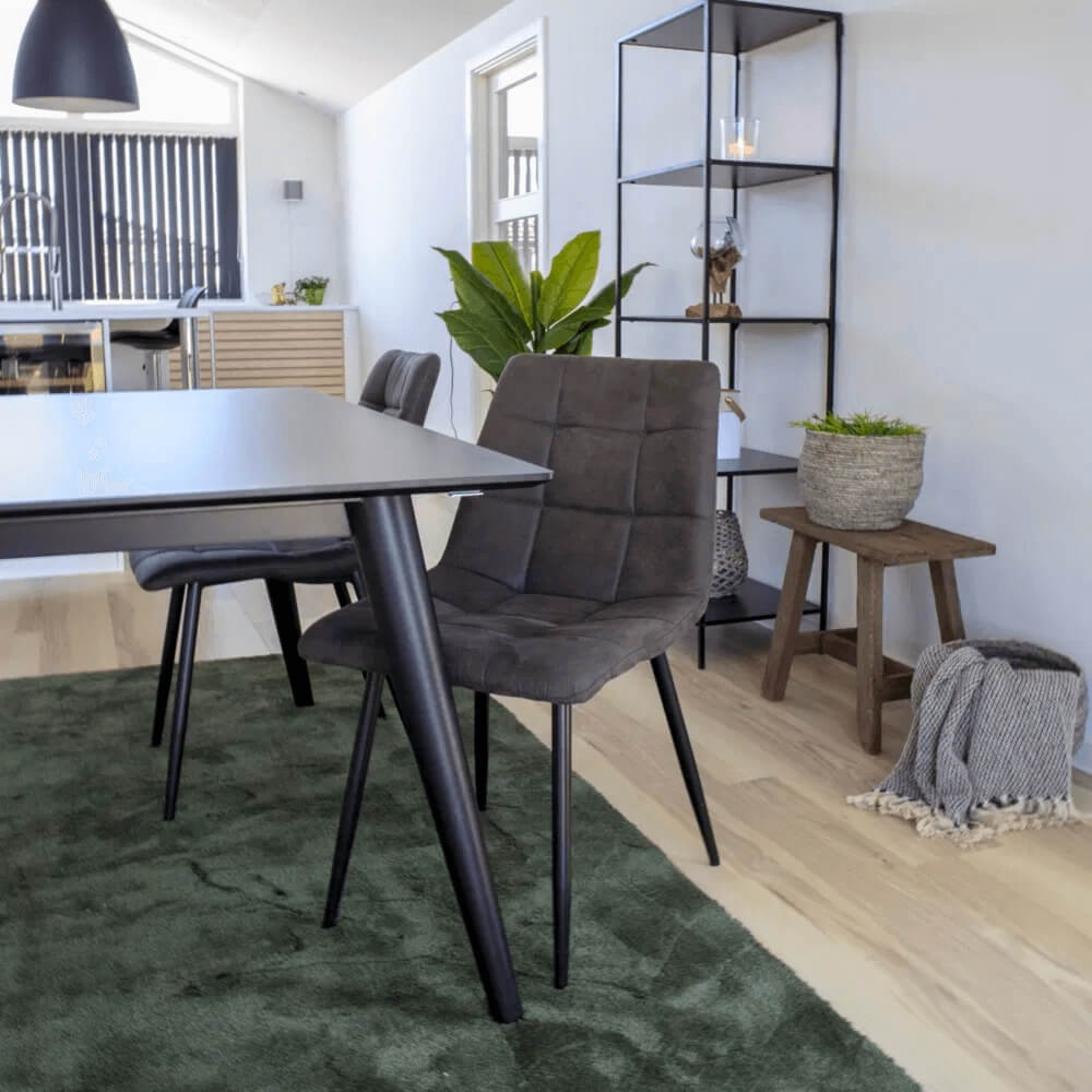 House Nordic Middelfart eetkamerstoel in donkergrijs microvezel met zwarte poten aan zwarte eettafel op groen vloerkleed in modern interieur.
