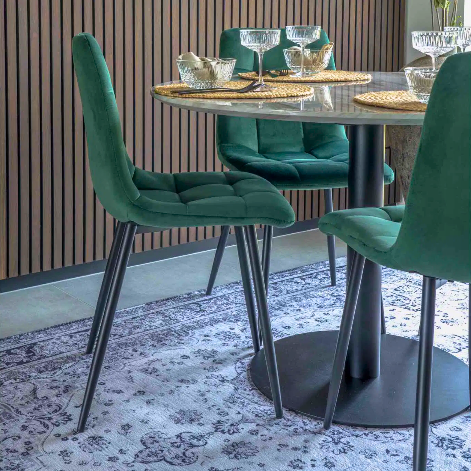 Close-up van House Nordic Middelfart eetkamerstoelen in donkergroen velvet met zwarte poten rond een moderne ronde eettafel in Scandinavische eetkamer.