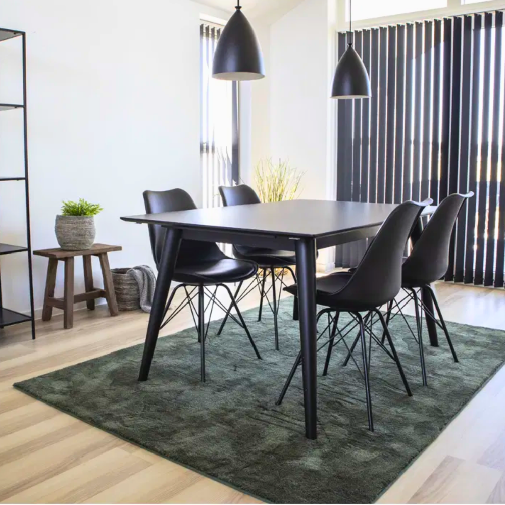 Moderne eetkamer met zwarte House Nordic Oslo eetkamerstoelen rond een zwarte tafel op een groen vloerkleed in Scandinavisch interieur.