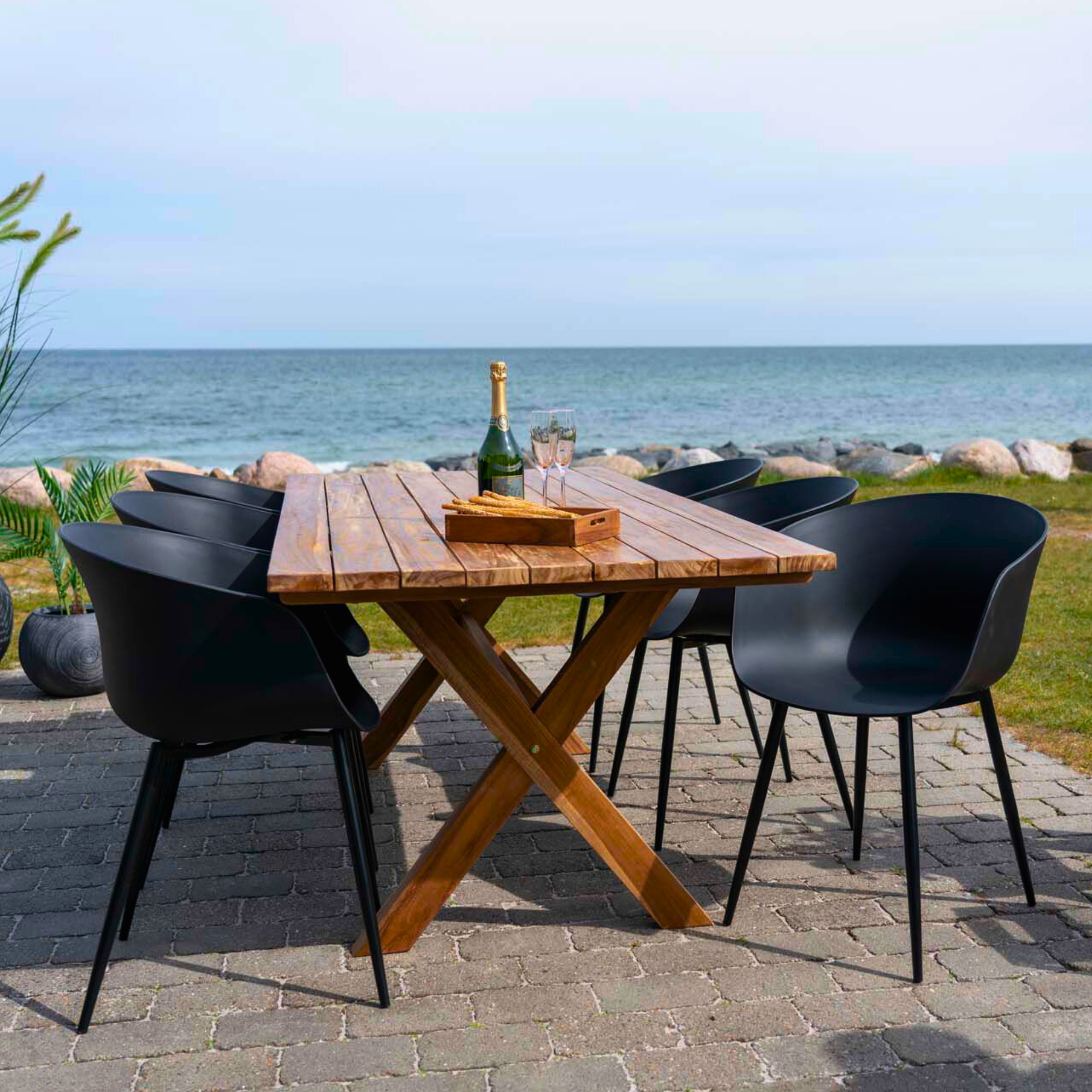 Zwarte House Nordic Roda eetkamerstoelen rond houten buitentafel met uitzicht op zee – Scandinavisch design voor terras of tuin.