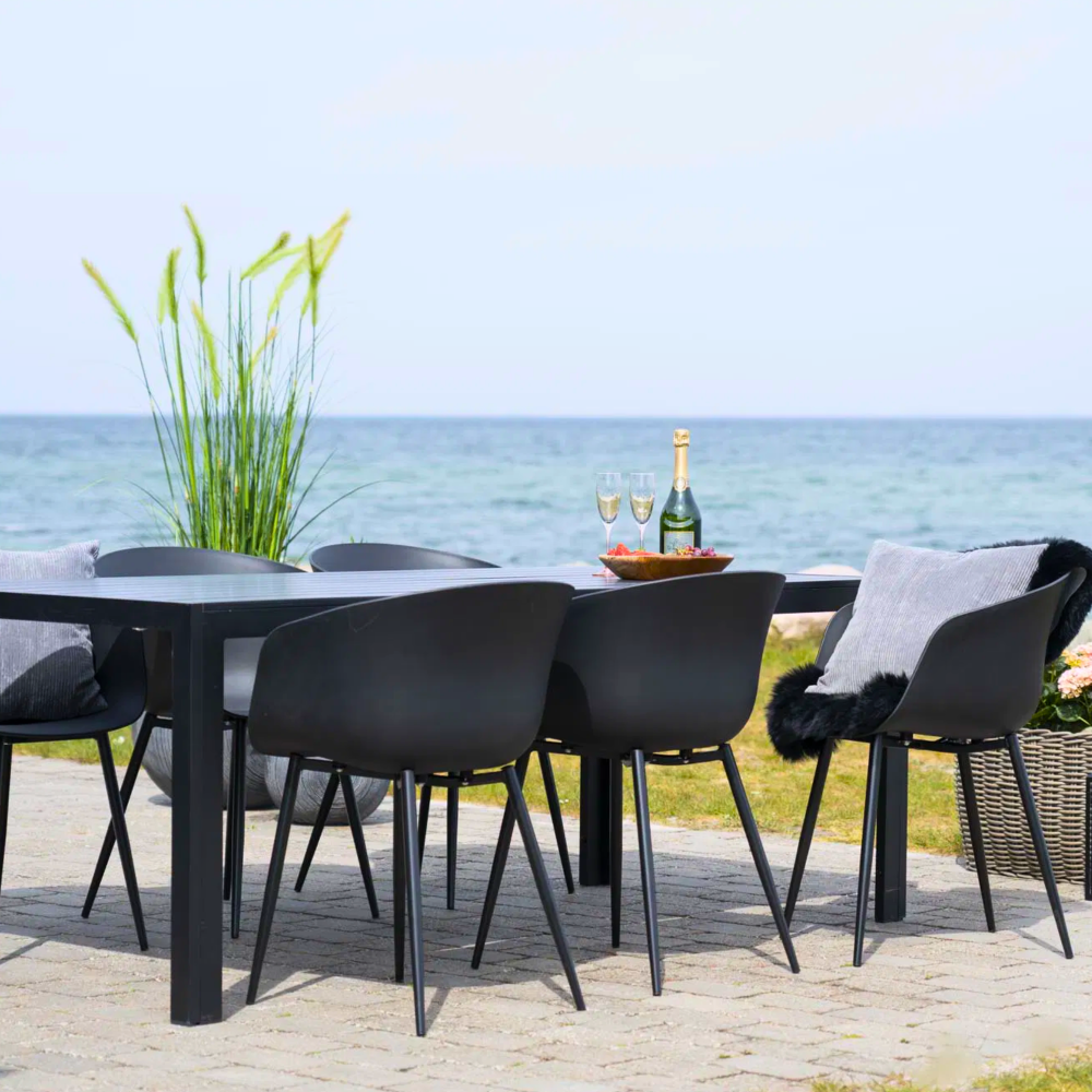 Set van zwarte House Nordic Roda eetkamerstoelen aan buitentafel met uitzicht op zee – elegant Scandinavisch design voor terras of tuin.
