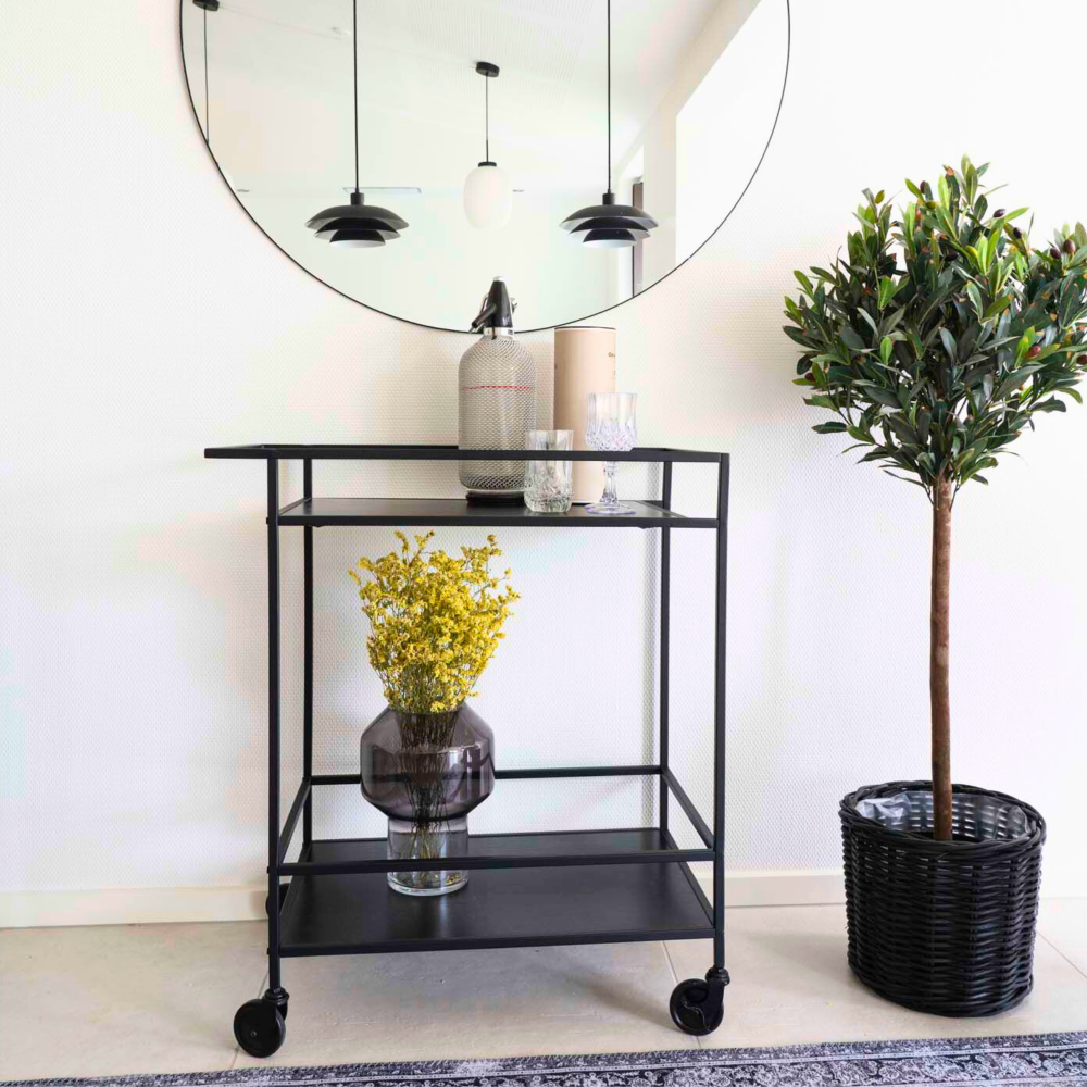 House Nordic Vita serveerwagen in zwart met bloemenvaas, glazen en decoratie in Scandinavisch interieur met spiegel en kamerplant.
