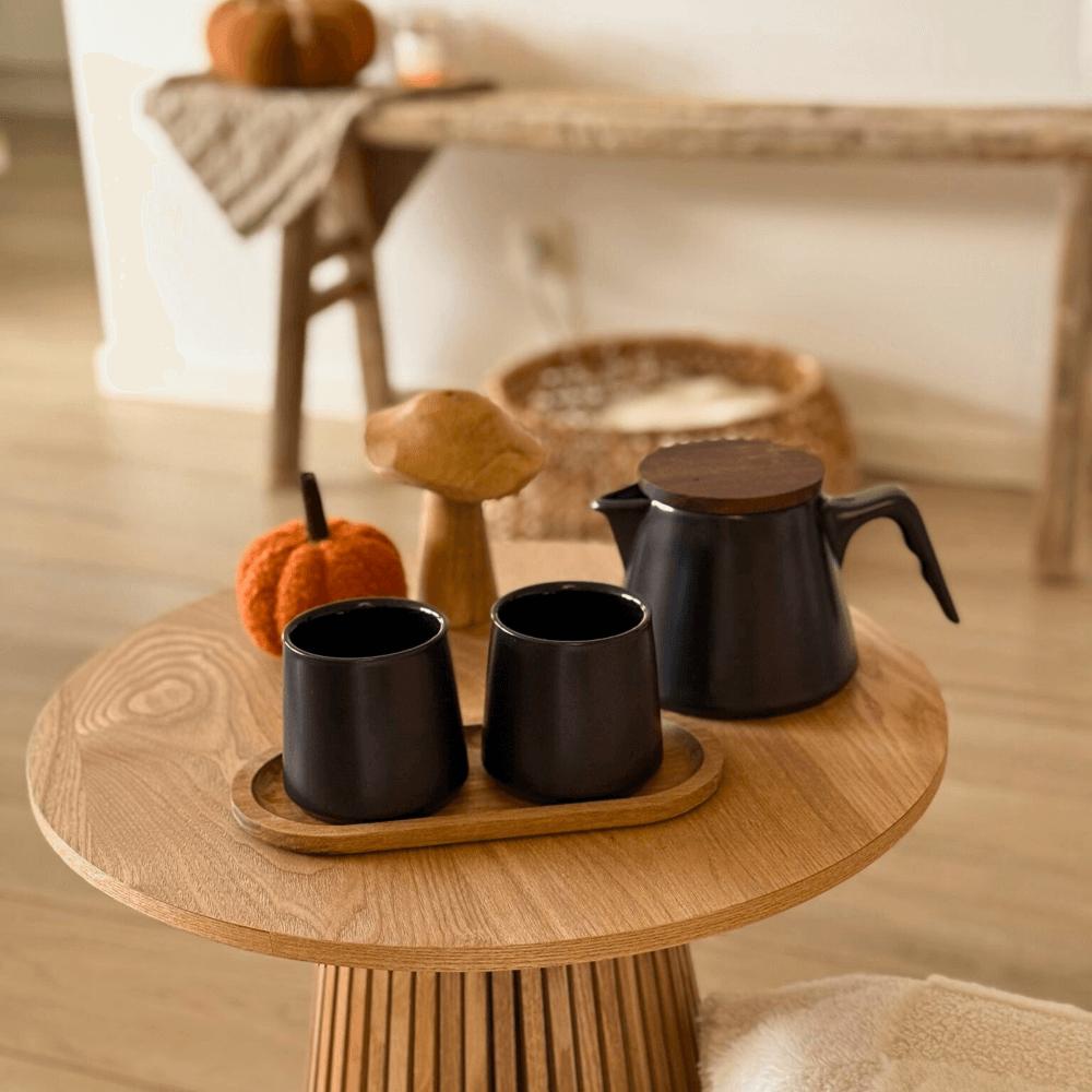 Zwarte design theeset van keramiek op houten bijzettafel in een warme, sfeervolle interieursetting. 