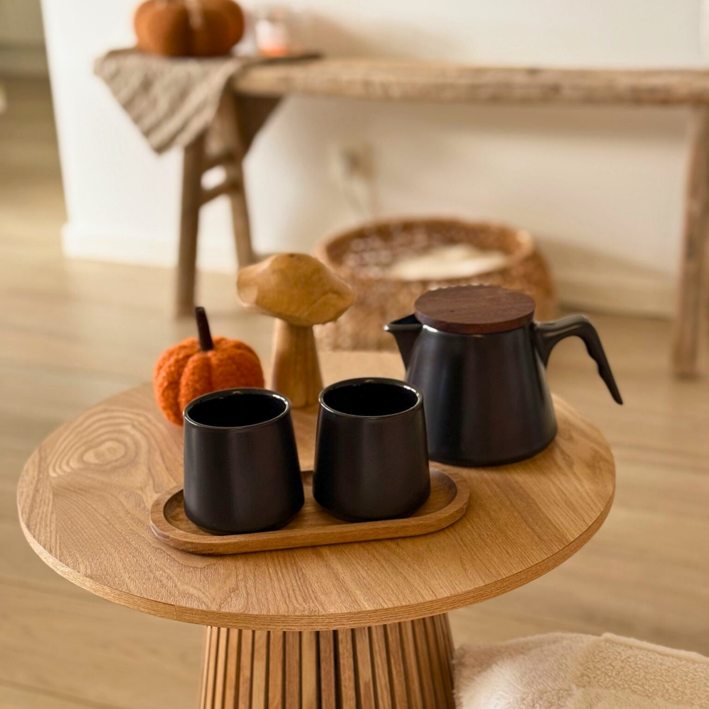 Zwarte design theeset van keramiek op houten bijzettafel in een warme, sfeervolle interieursetting. 