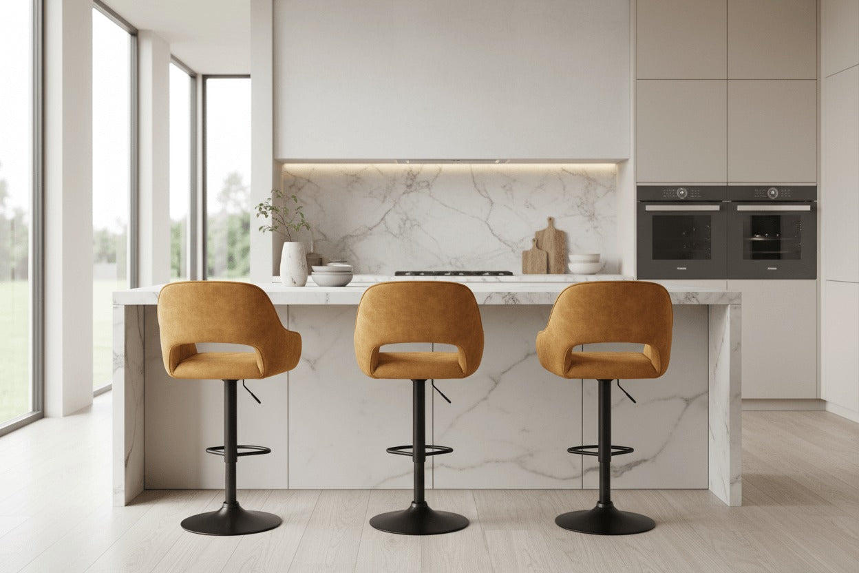 Meerdere RV Design Katy barkrukken in Aurora velours goud aan een luxe keuken met marmeren kookeiland en zwart metalen onderstel.