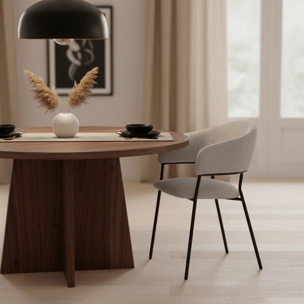 RV Design Liam armstoel in lichtgrijze stof naast een ronde houten eettafel in een warme, sfeervolle eetkamer.