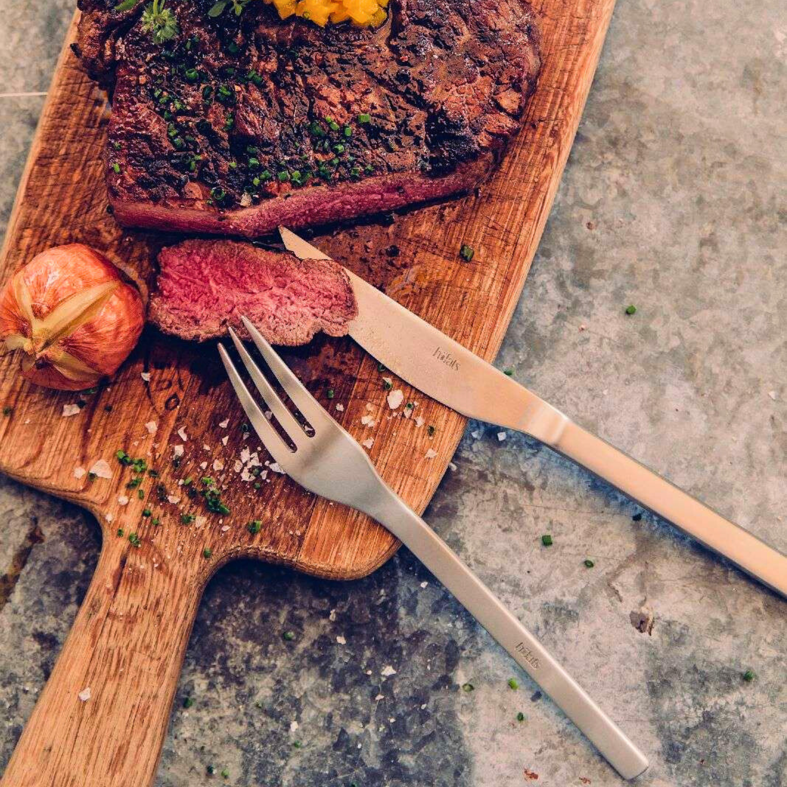 Luxe RVS steak bestekset van Höfats – steakmes en vork gebruikt bij perfect gebakken steak op houten serveerplank.