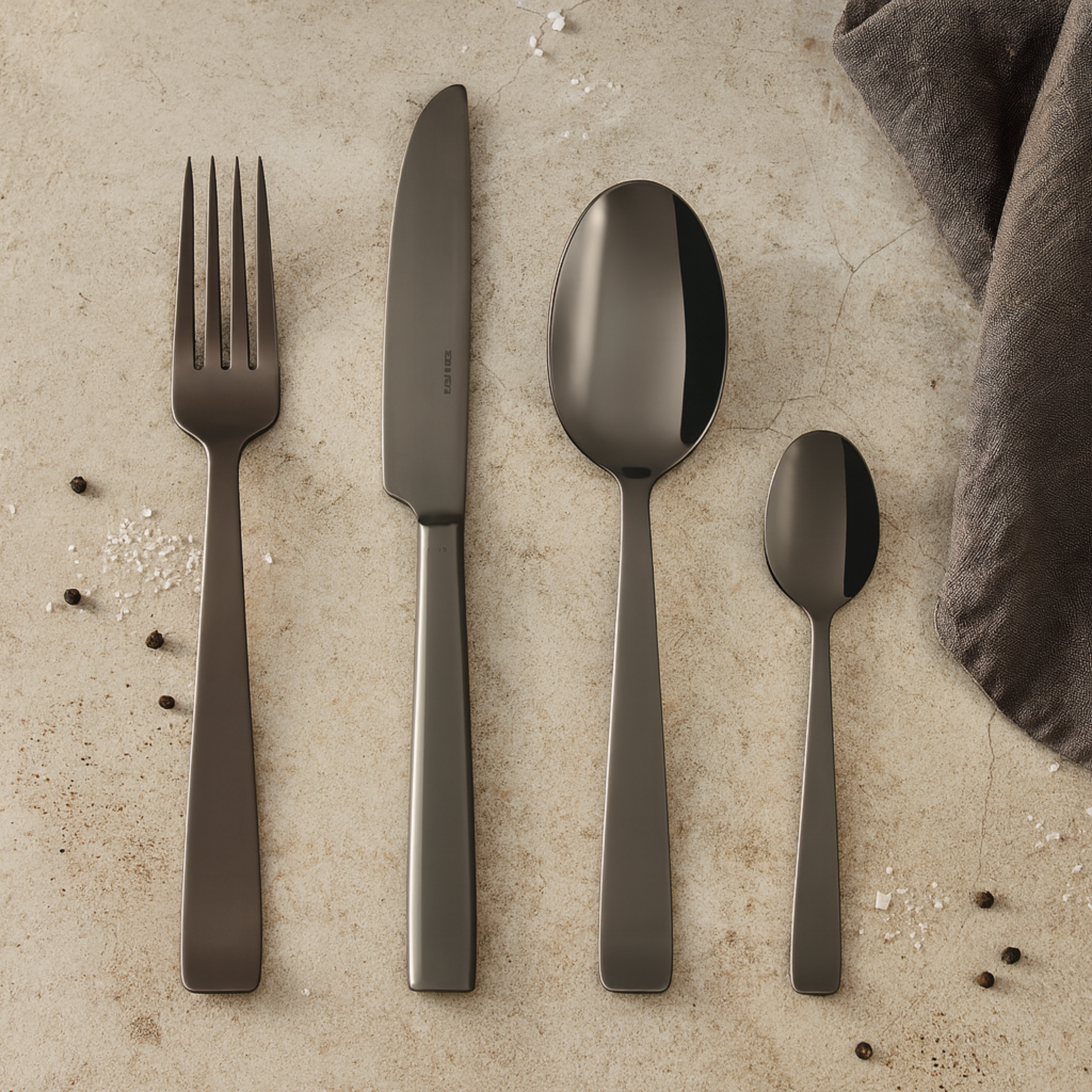 Sambonet Flat PVD bestekset 24-delig in zwart – stijlvol gepresenteerd op tafel met peperkorrels en zoutkorrels.