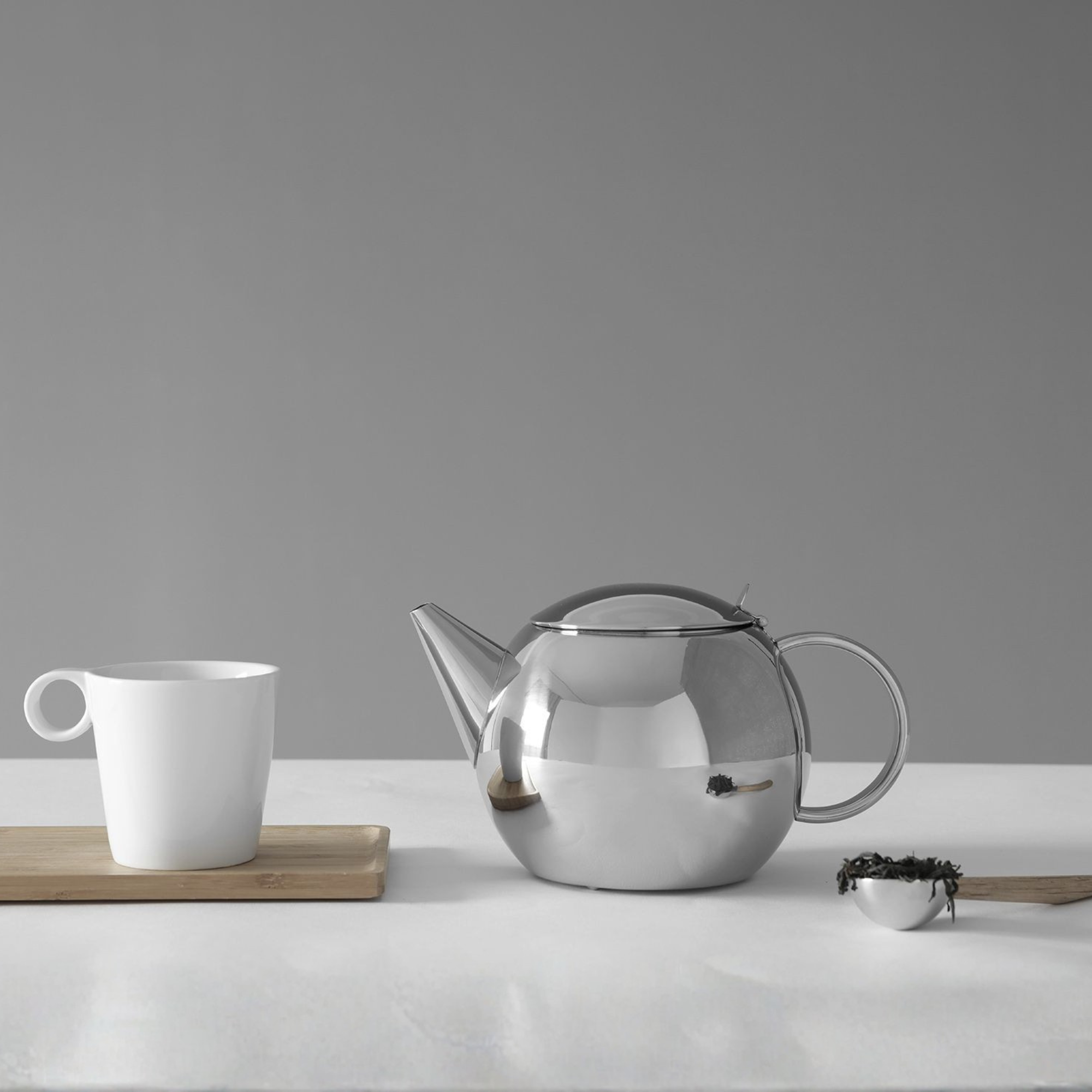 Viva Scandinavia Lucas theepot van roestvrij staal op tafel naast witte mok en theeblaadjes – Scandinavisch design.